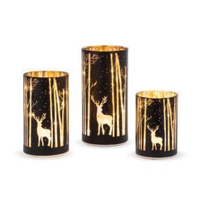 A set of three light up hurricane lights with silhouette images of deer in the forest.
