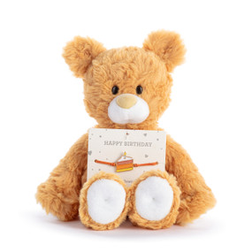 An orange plush teddy bear with an attached birthday bracelet with a slice of cake intended for a child.