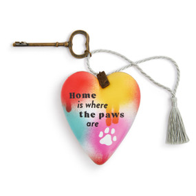 A colorful heart shaped sculpture with bright spots of paint, a paw print and the saying "Home is where the paws are". The heart has a metal key and silver tassel.