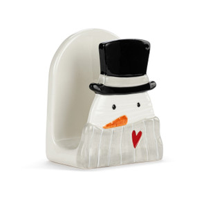 A cream ceramic napkin holder with a snowman on the front with a black top hat and gray scarf displayed at an angle to show the opening.