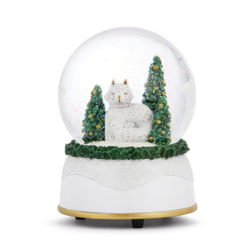 A musical snow globe with a white base and a white fox sitting with two decorated trees inside.
