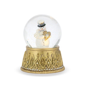 A lit snow globe with a gold base and a glittery snowman holding a gold heart with a silver snowflake inside.