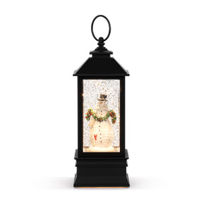 A black lit musical lantern with snowman figure inside holding a green decorated swag.