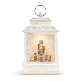 A white lit musical lantern with the image of a Nutcracker standing among the trees inside.