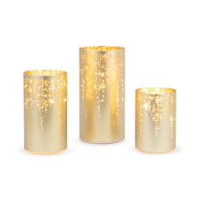 A set of three gold light up hurricane lights with cut out stars coming down from the top.