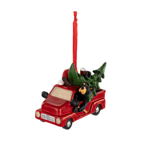 An ornament of a black bear driving a red truck with a large Christmas tree in the back, hanging from a red ribbon.