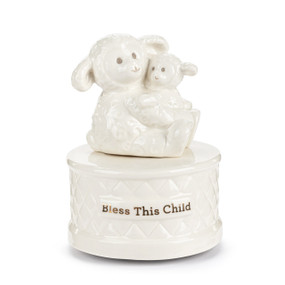 A white ceramic music box with a lamb holding a baby lamb in its lap. The base has "Bless This Child" in gold.