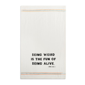 A white kitchen towel with the saying "Being weird is the fun of being alive" displayed laid out flat.