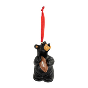 An ornament of a black bear playing with a football. The ornament has a red ribbon hanger.