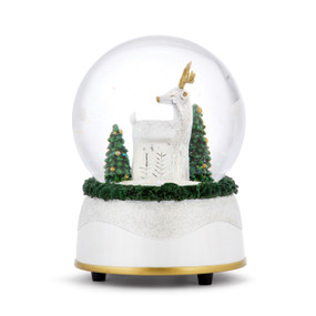 A musical snow globe with a white base and a white deer standing with two decorated trees inside.