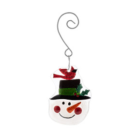 A white and red glass ornament of a Snowmans face wearing a top hat with a cardinal perched on it. The ornament has a curved silver hanger.