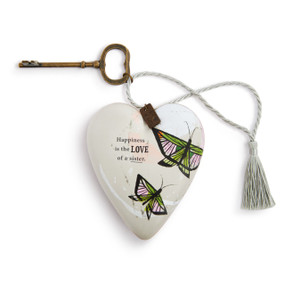 A cream heart shaped sculpture with two pink and green butterflies and the saying "Happiness is the Love of a sister". The heart has a metal key and silver tassel.