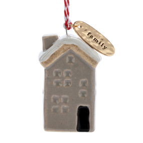 A small ceramic tan house shaped ornament with snow on the roof and a gold metal tag at the top with the word "family".