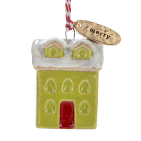 A small ceramic green house shaped ornament with snow on the roof and a gold metal tag at the top with the word "merry".