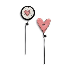 Two black metal plant stakes. There is a decorative ceramic pink heart on one and a black and white circle with a pink heart in the middle of the other.