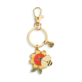 A gold keychain with two charms. One is a small gold circle with the saying "Bee Kind" and the other is a flower with a bee.