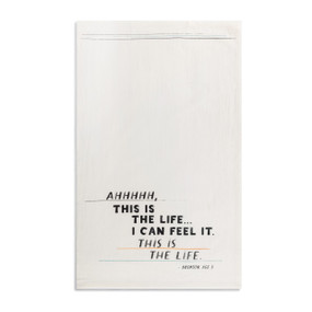 A white kitchen towel with the saying "AHHHH, this is the life...I can feel it. This is the life" displayed laid out flat.