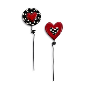 Two black metal plant stakes. There is a decorative ceramic red heart on one and a black and white check circle with a red heart in the middle of the other.