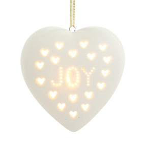 A heart shaped white ceramic light up ornament with small white heart cutouts and the word "Joy" displayed lit.