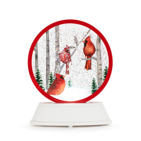 A round disc shaped snow globe perched on a white base. Inside the globe is an image of three cardinal birds in a snowy forest.