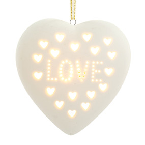 A heart shaped white ceramic light up ornament with small white heart cutouts and the word "Love" displayed lit.