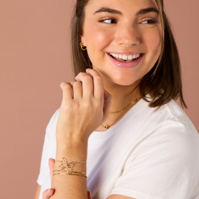 A smiling woman wearing a gold chain bracelet with a open work butterfly charm.