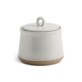 A himalayan citrus candle in a short white ceramic jar with a lid and tan textured base.