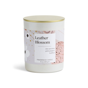 An 8 oz leather blossom scented candle in a round white container with a gold lid.