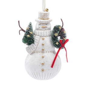 A white paper pulp snowman ornament  in a top hat and scarf. He has a green wreath in one arm and a small green tree in the other.