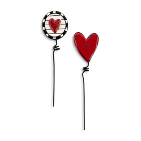 Two black metal plant stakes. There is a decorative ceramic red heart on one and a black and white circle with a red heart in the middle of the other.