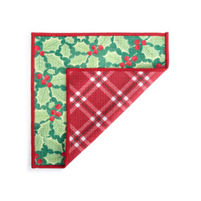 A double sided square dish cloth that is green with holly illustrations on one side and red plaid on the other displayed with the red corner turned back.