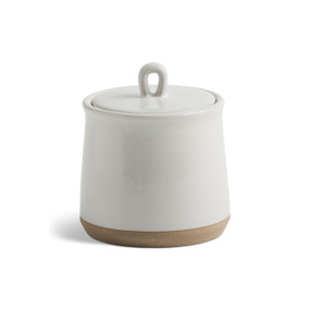 A himalayan citrus candle in a medium white ceramic jar with a lid and tan textured base.