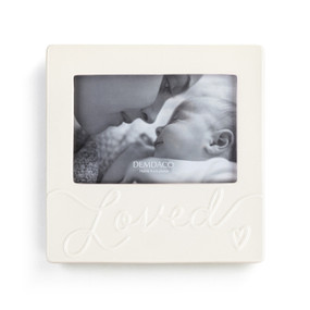 A cream ceramic photo frame holding a 4x6 photo that has the word "Loved" and a heart in raised letters on the front bottom half.
