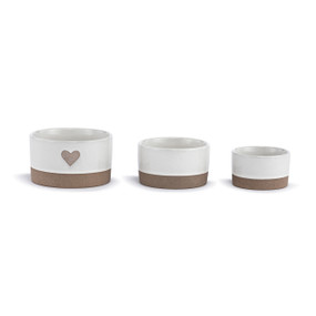 A set of three small white ceramic nesting bowls with tan textured bases and a heart on the largest.