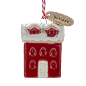 A small ceramic red house shaped ornament with snow on the roof and a gold metal tag at the top with the word "believe".