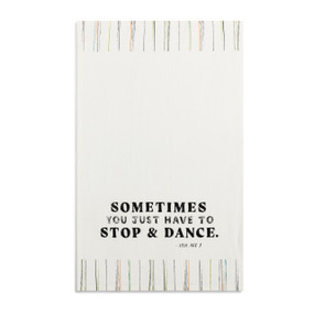 A white kitchen towel with the saying "Sometimes you just have to stop & dance" displayed laid out flat.