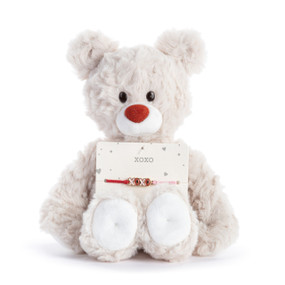 A cream plush teddy bear with an attached bracelet with a XOXO charm intended for a child.