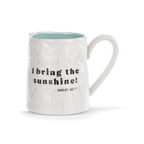 A white ceramic mug with a crinkly appearance. The interior is light blue and the saying "I bring the sunshine" is on the front.