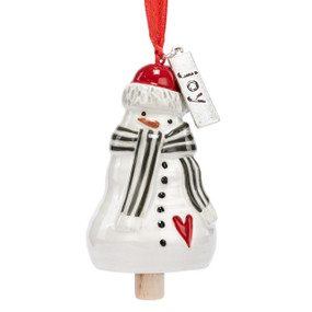 A small white bell shaped like a snowman wearing a black and white striped scarf and has a silver metal tag with the word "joy" at the top.