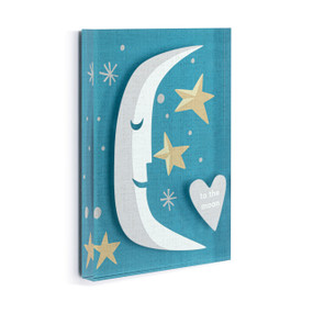 A blue acrylic wall art tile with an illustrated smiling crescent moon and stars with the saying "to the moon" displayed angled to the right.