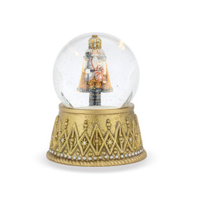 A lit snow globe with a decorative gold base and a sparkly nutcracker in gold and blue inside.