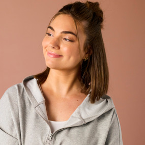 A young woman wears a gray poncho with a half zipper and a hood in the back