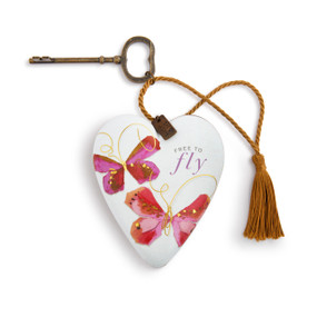 A white heart shaped sculpture with pink butterflies and the saying "Free to fly". The heart has a metal key and gold tassel.