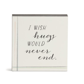 A white wall art with the saying "I wish hugs would never end."