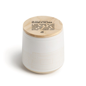 A white ceramic jar candle. The lid is wood with the saying "RE: Out of the Office Relaxing at the cabin" with a short write up about someone at the cabin.