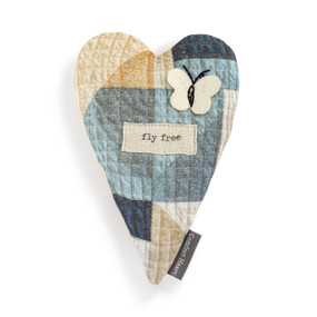 Top down view of a heart shaped pillow. The pillow has fabric with blocks of blue, yellow and natural colored fabric like a patchwork quilt. There is a patch shaped like a butterfly in the upper right, above another patch with the phrase "fly free" printed in typeface.