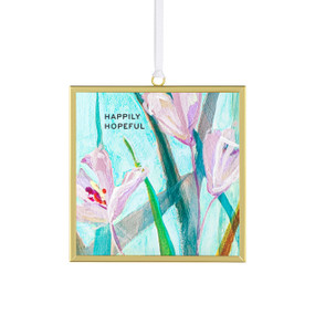 Front view of a glass suncatcher in a gold frame with a white cord threaded through a loop hanger on the top. On the surface of the glass is print of pink flowers and green leaves on a sky blue background. "Happily hopeful" is printed on the upper right corner.