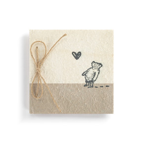 Top down view of the front cover of a beige and brown paper mâché journal. The cover has an illustration of classic Winnie-the-Pooh looking at a heart shaped butterfly. The journal is bound with twine on the left side.