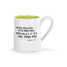 Front view of a white ceramic mug with green interior, with the handle on the right. The mug's surface resembles a smoothed-out piece of crumpled notepaper. Text on the mug reads, "Always follow your dreams...especially if it's for your dog."