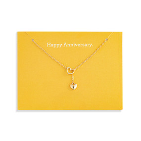 Top down view of a gold necklace with a gold heart charm attached to a yellow card. "Happy Anniversary" is printed on the card above the necklace.